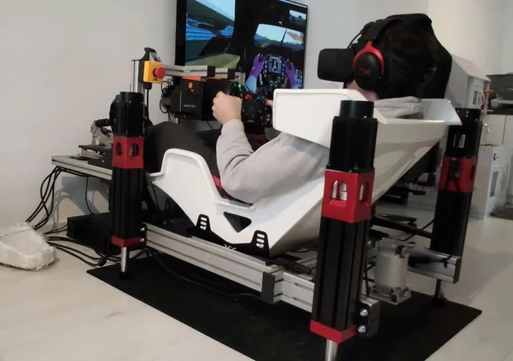 An aluminium-profile racing rig with four red-and-black motion actuators and a white formula seat.